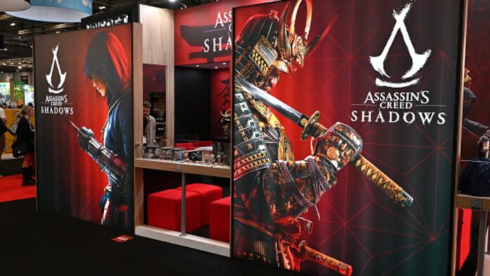 ภาพบูธจัดแสดงเกม Assassin’s Creed Shadows ภายในงานเกมโชว์ โดดเด่นด้วยโปสเตอร์ขนาดใหญ่ของตัวละครซามูไรและนักฆ่าหญิง