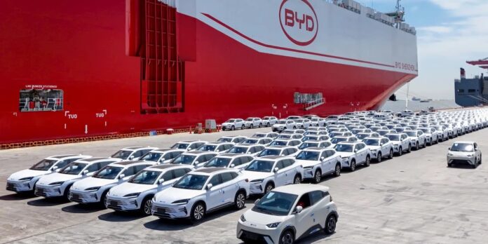 ภาพเรือขนส่งรถยนต์ขนาดใหญ่ของบริษัท BYD พร้อมกับรถยนต์รุ่นต่างๆ จอดเรียงรายอยู่ด้านหน้า