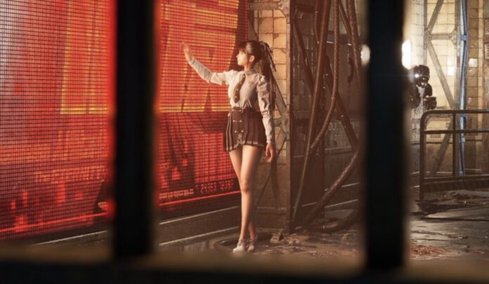 ตัวละคร Eve ในชุดยูนิฟอร์มสไตล์แฟชั่นยืนอยู่หน้าจอแสดงผลขนาดใหญ่สีแดงในฉากแนวไซไฟ