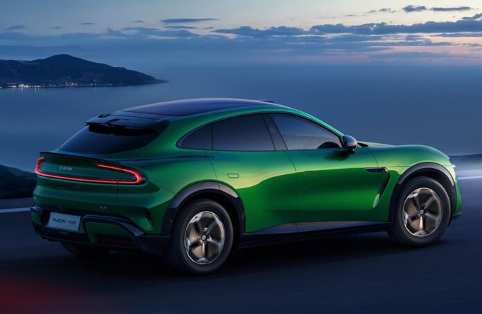 มุมมองด้านหลังของรถยนต์ไฟฟ้า Xiaomi YU7 สีเขียว ขณะวิ่งบนถนนริมทะเลในช่วงพระอาทิตย์ตก เผยให้เห็นดีไซน์แบบ SUV คูเป้