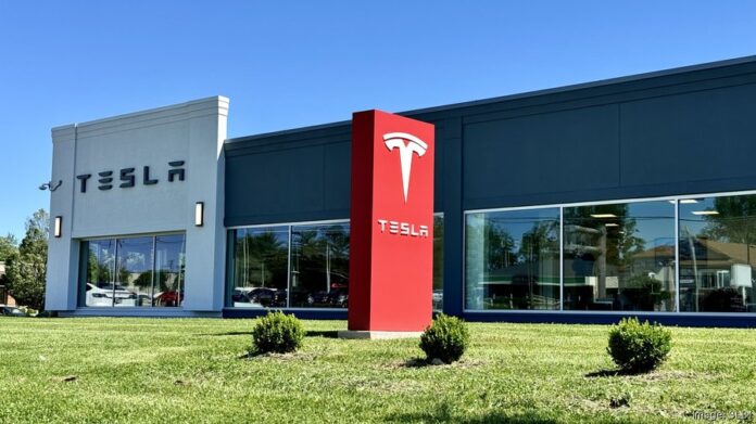 ศูนย์บริการ Tesla พร้อมป้ายโลโก้สีแดงโดดเด่นตั้งอยู่ด้านหน้าตึก มีพื้นหญ้าเขียวขจีและท้องฟ้าแจ่มใส