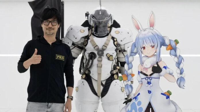 Hideo Kojima ใส่แว่นยืนชูนิ้วโป้งข้างชุดเกราะหุ่นยนต์สีขาว พร้อม Usada Pekora VTuber สาว