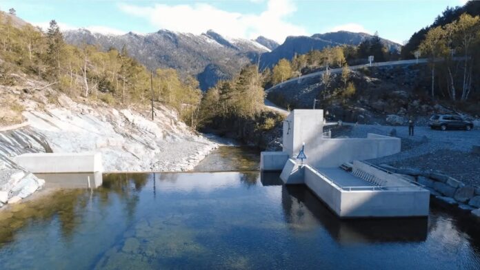 เขื่อนขนาดเล็กสำหรับพลังน้ำ ตั้งอยู่กลางหุบเขา มีน้ำไหลผ่านโครงสร้างคอนกรีต ล้อมรอบด้วยภูเขาและต้นไม้
