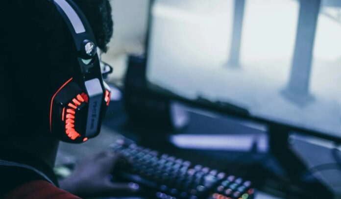 ผู้เล่นสวมชุดหูฟังเล่นเกมบนคอมพิวเตอร์หน้าจอใหญ่พร้อมคีย์บอร์ดมีไฟ RGB