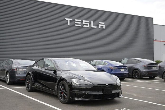 รถยนต์ Tesla หลายคันจอดอยู่หน้าอาคารที่มีโลโก้ TESLA ขนาดใหญ่
