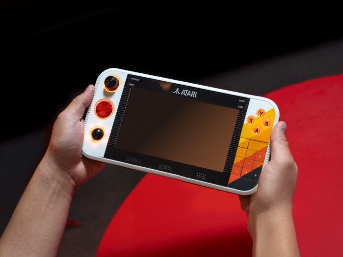 ภาพเครื่องเล่นเกมพกพา Atari Gamestation Go โดยมีมือสองข้างถือเครื่องอยู่