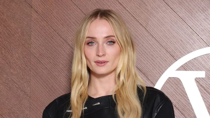 ภาพ Sophie Turner มองตรงมาด้านหน้าส่งยิ้มให้กล้องเล็กน้อย
