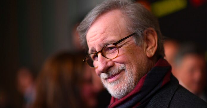 Steven Spielberg ผู้กำกับภาพยนตร์ชื่อดังสวมแว่นตา กำลังยิ้มมุมปากพร้อมหันหน้าเล็กน้อยในงานอีเวนต์