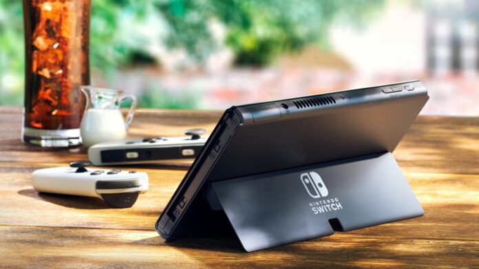 คอนโซล Nintendo Switch รุ่นหน้าจอ OLED วางอยู่บนโต๊ะไม้กลางแจ้ง โดยกางขาตั้งด้านหลังออกมา