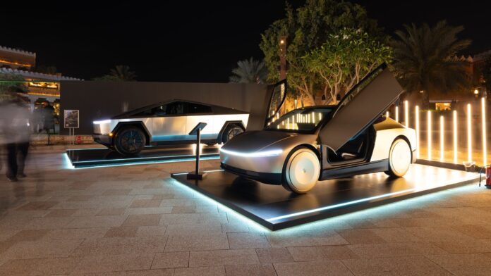 รถยนต์ต้นแบบ Tesla Cybercab จอดโชว์คู่กับ Tesla Cybertruck บนแท่นจัดแสดงกลางแจ้งในเวลากลางคืน ที่มีแสงไฟส่องพื้นรอบตัวรถ