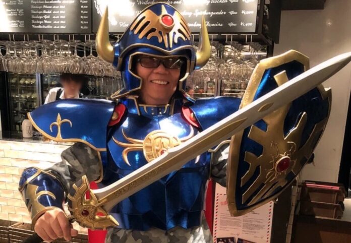 Yuji Horii ผู้สร้างเกม Dragon Quest สวมชุดเกราะพร้อมถือดาบและโล่ ท่ามกลางบรรยากาศงานเฉลิมฉลอง