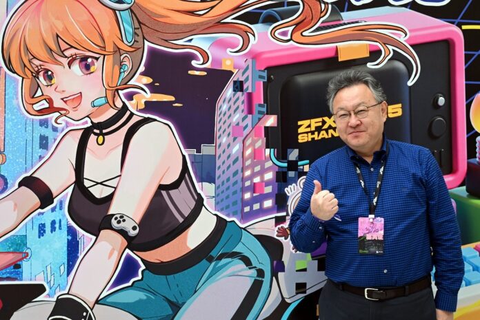 Shuhei Yoshida ยืนถ่ายรูปหน้างาน WePlay Expo 2025 โดยมีภาพตัวละครอนิเมะอยู่ด้านหลัง