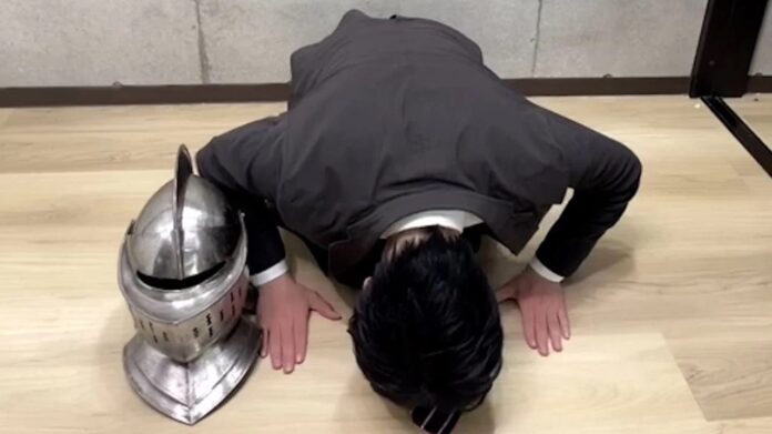 Narunii YouTuber ชาวญี่ปุ่นก้มศีรษะขอโทษ พร้อมหมวกอัศวิน Dark Souls วางอยู่ข้างหน้า สื่อถึงการออกมาแสดงความรับผิดชอบต่อปัญหาการพัฒนาเกม Chikai no Fuchi