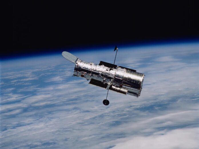 กล้องโทรทรรศน์อวกาศ Hubble ลอยอยู่ในวงโคจรรอบโลก เหนือชั้นบรรยากาศของโลกที่มองเห็นเป็นสีฟ้า