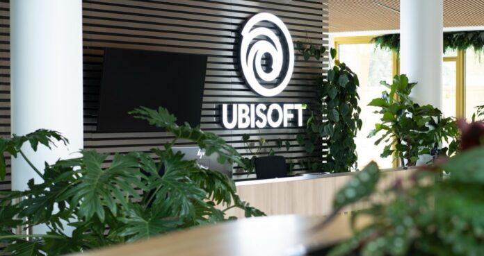 โลโก้ Ubisoft ติดตั้งอยู่ภายในสำนักงาน พร้อมต้นไม้ประดับและพื้นที่ทำงานด้านหน้า