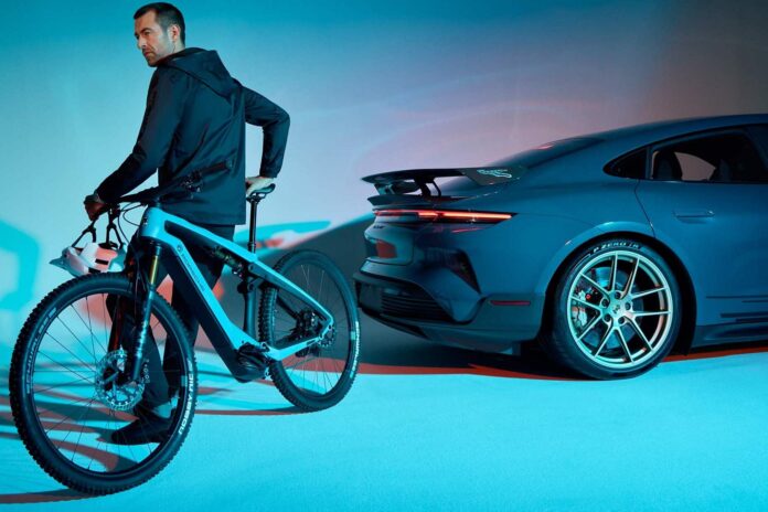 ผู้ชายกำลังนั่งบนจักรยานไฟฟ้าโดยมีรถสปอร์ต Porsche จอดอยู่ด้านหลัง
