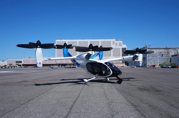 แท็กซี่อากาศยานไฟฟ้า eVTOL จอดอยู่บนลานบินด้านหน้าอาคาร ภายใต้ท้องฟ้าสีคราม