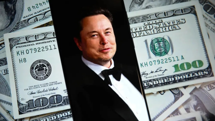 ภาพ Elon Musk บนหน้าจอสมาร์ตโฟน วางบนพื้นหลังธนบัตรดอลลาร์สหรัฐ สื่อถึงความมั่งคั่งระดับมหาศาลและการก้าวขึ้นเป็นมหาเศรษฐีล้านล้านดอลลาร์คนแรกของโลก