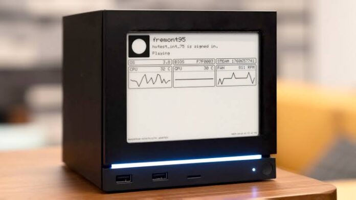 Steam Machine สีดำพร้อมหน้ากากจอ e-ink แสดงข้อมูลระบบ วางอยู่บนโต๊ะไม้