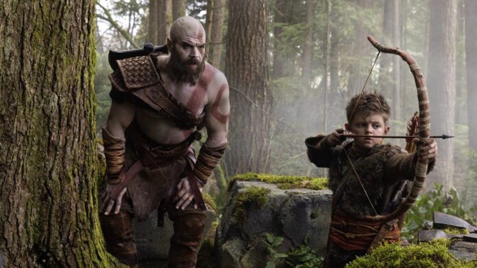 Kratos ยืนอยู่ข้าง Atreus ที่กำลังเล็งธนูในป่าระหว่างฉากจากซีรีส์ God of War ฉบับคนแสดง