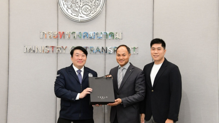 ผู้แทนกระทรวงคมนาคมและ Tesla ยืนถ่ายภาพร่วมกัน พร้อมถือกล่องของที่ระลึก Tesla ภายในกระทรวงคมนาคม