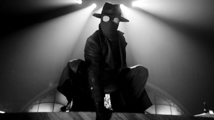 Spider-Man Noir ในชุดโค้ตยาวและหมวกเฟโดราสีดำ กำลังย่อตัวเตรียมพร้อมในบรรยากาศโทนขาวดำ