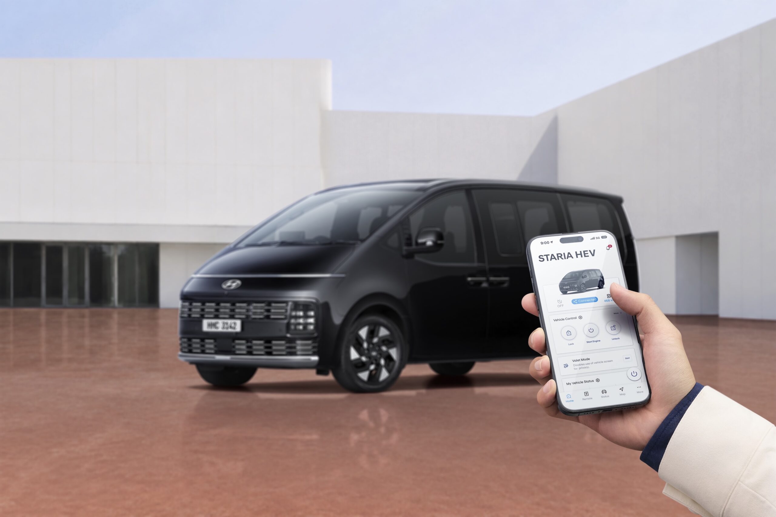 สมาร์ตโฟนแสดงแอป Hyundai Bluelink โดยมี STARIA Hybrid อยู่ด้านหลัง