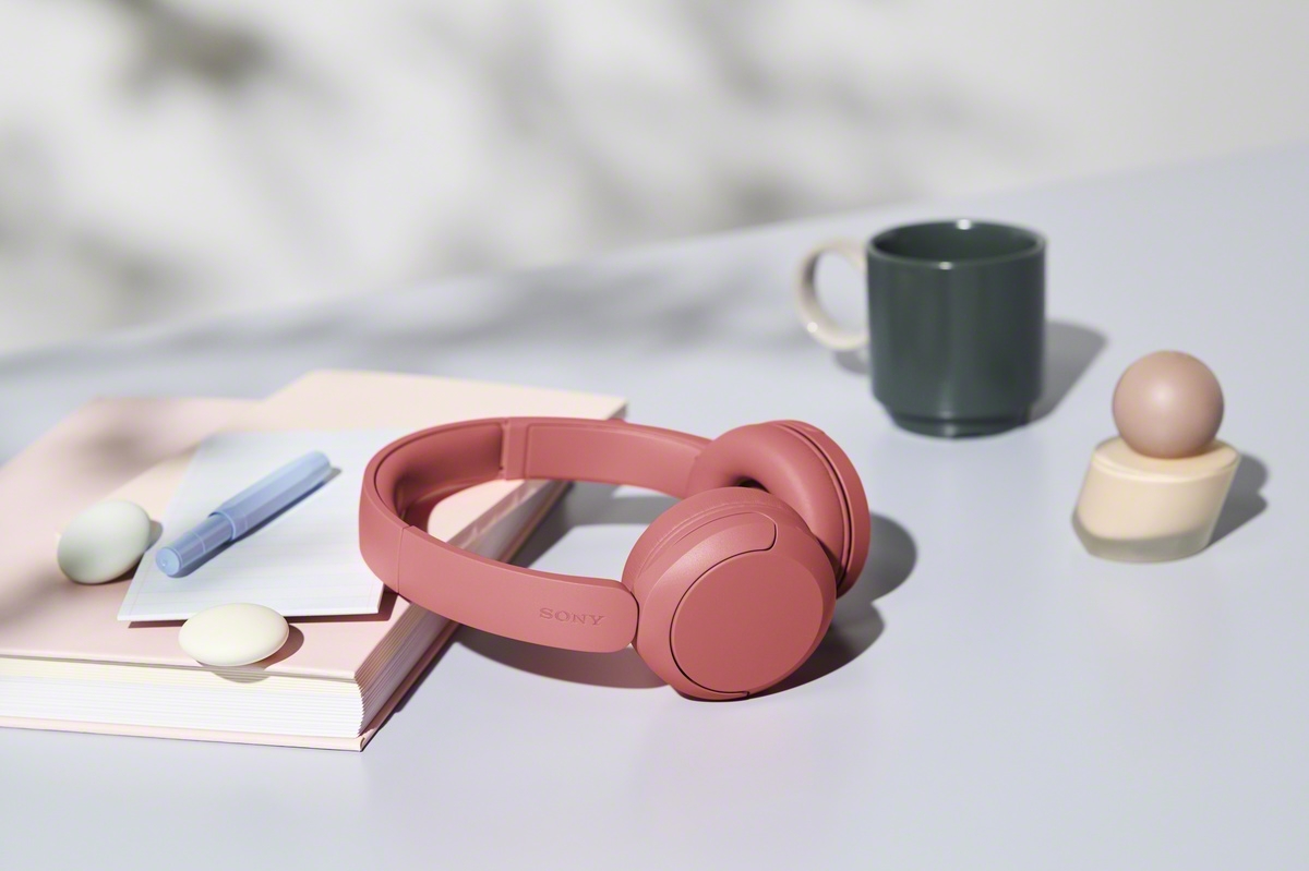 หูฟัง Sony WH-CH530 สี Coral วางอยู่บนโต๊ะข้างสมุดและแก้วน้ำ