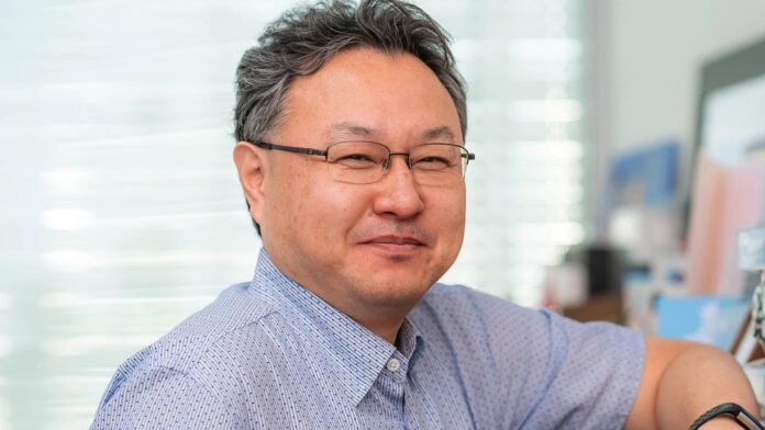 Shuhei Yoshida สวมแว่นตาและเสื้อเชิ้ตลายจุด ยิ้มให้กล้อง