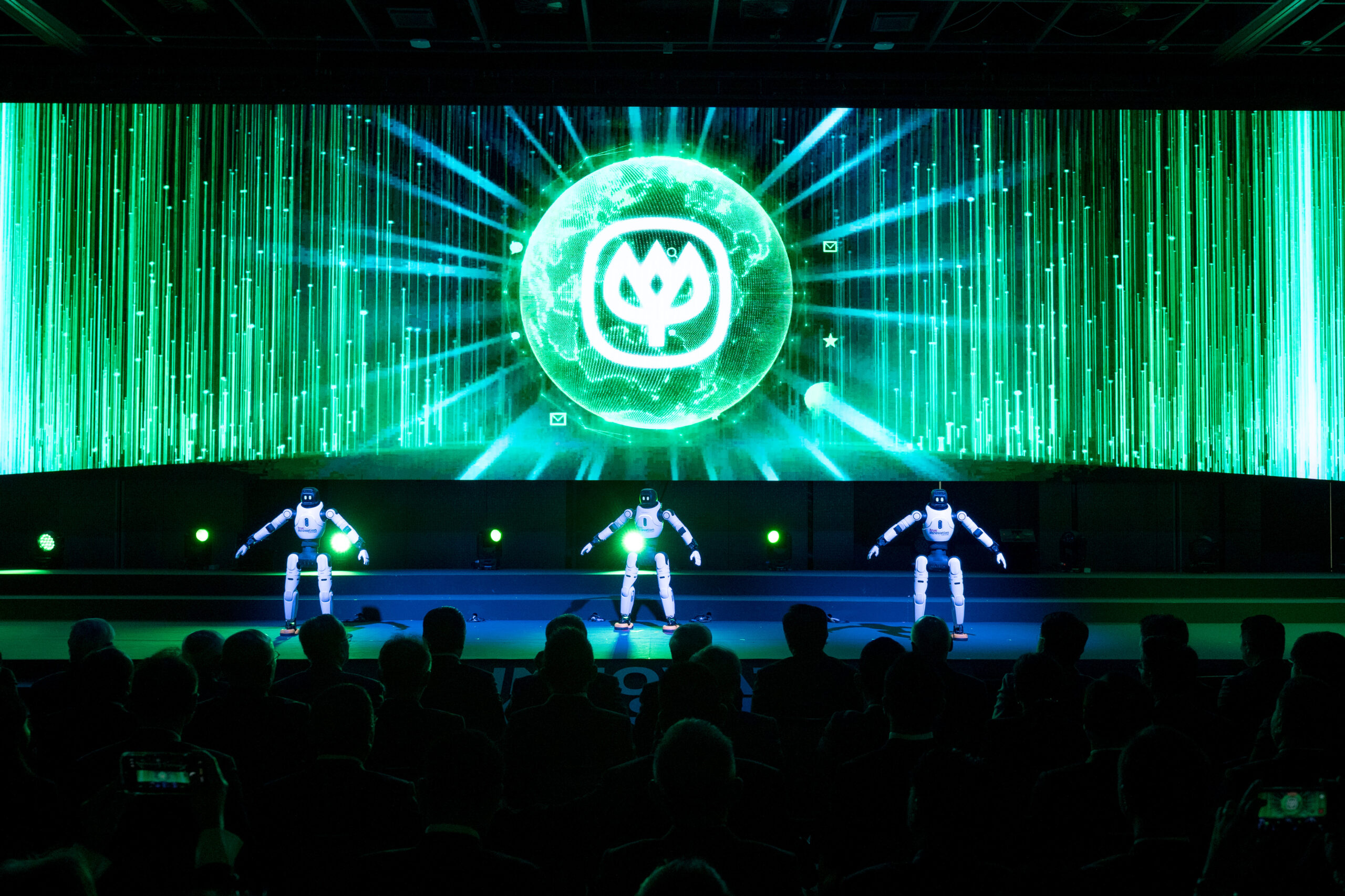 หุ่นยนต์สามตัวแสดงบนเวทีด้านหน้าจอโลโก้เครือซีพี