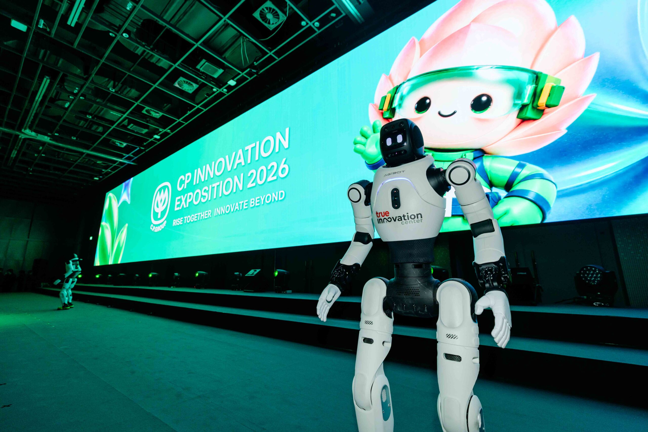 หุ่นยนต์ด้านหน้าเวทีที่มีชื่อ CP Innovation Exposition 2026 และมาสคอตบนจอ