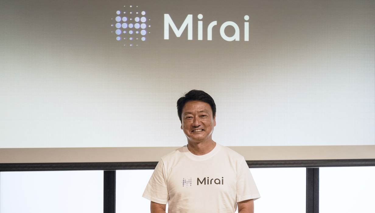 ยูสุเกะ โทมิโมโตะ ยืนหน้าโลโก้ Mirai ในงานเปิดตัว