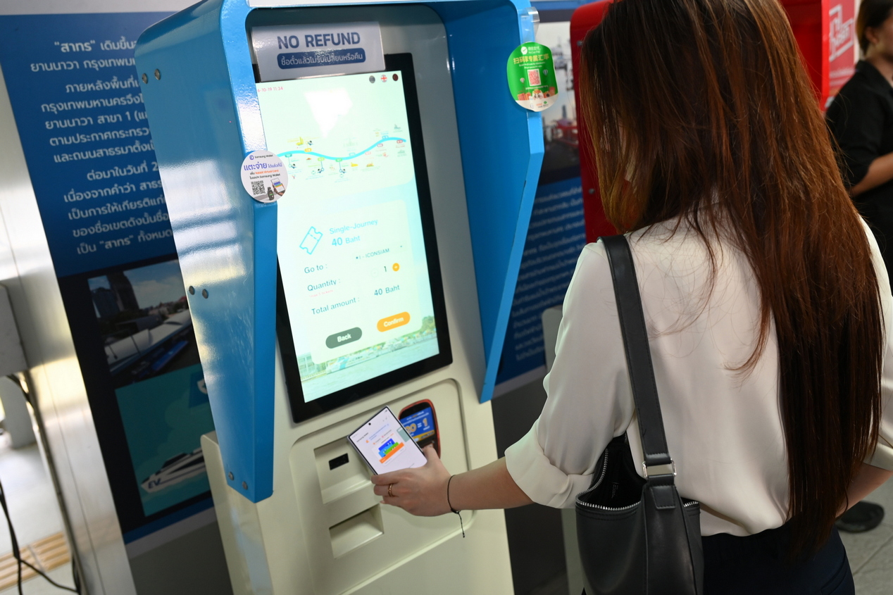 ผู้โดยสารใช้โทรศัพท์แตะเครื่องอ่านบัตรที่ตู้จำหน่ายตั๋วเรืออัตโนมัติ