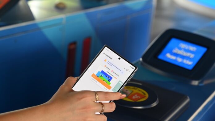 มือแตะโทรศัพท์ที่แสดง Rabbit Virtual Card ใน Samsung Wallet บนเครื่องอ่านบัตรทางเข้ารถไฟฟ้า