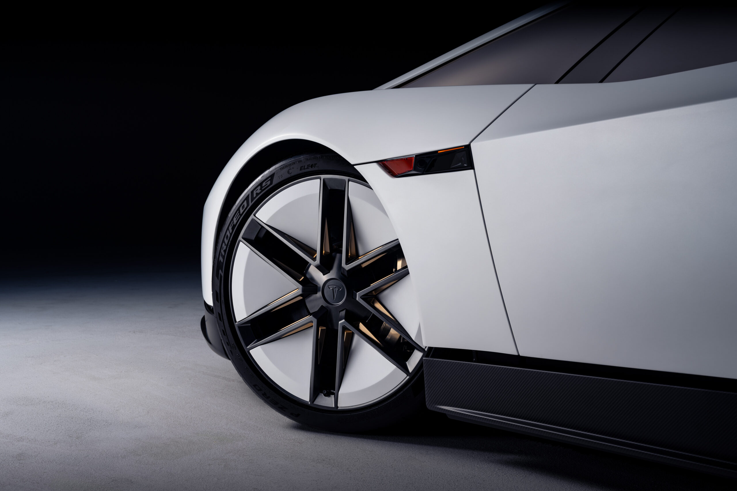 มุมใกล้ของล้อหน้าและตัวถังด้านข้าง Roadster เห็นโลโก้ Tesla บนดุมล้อ