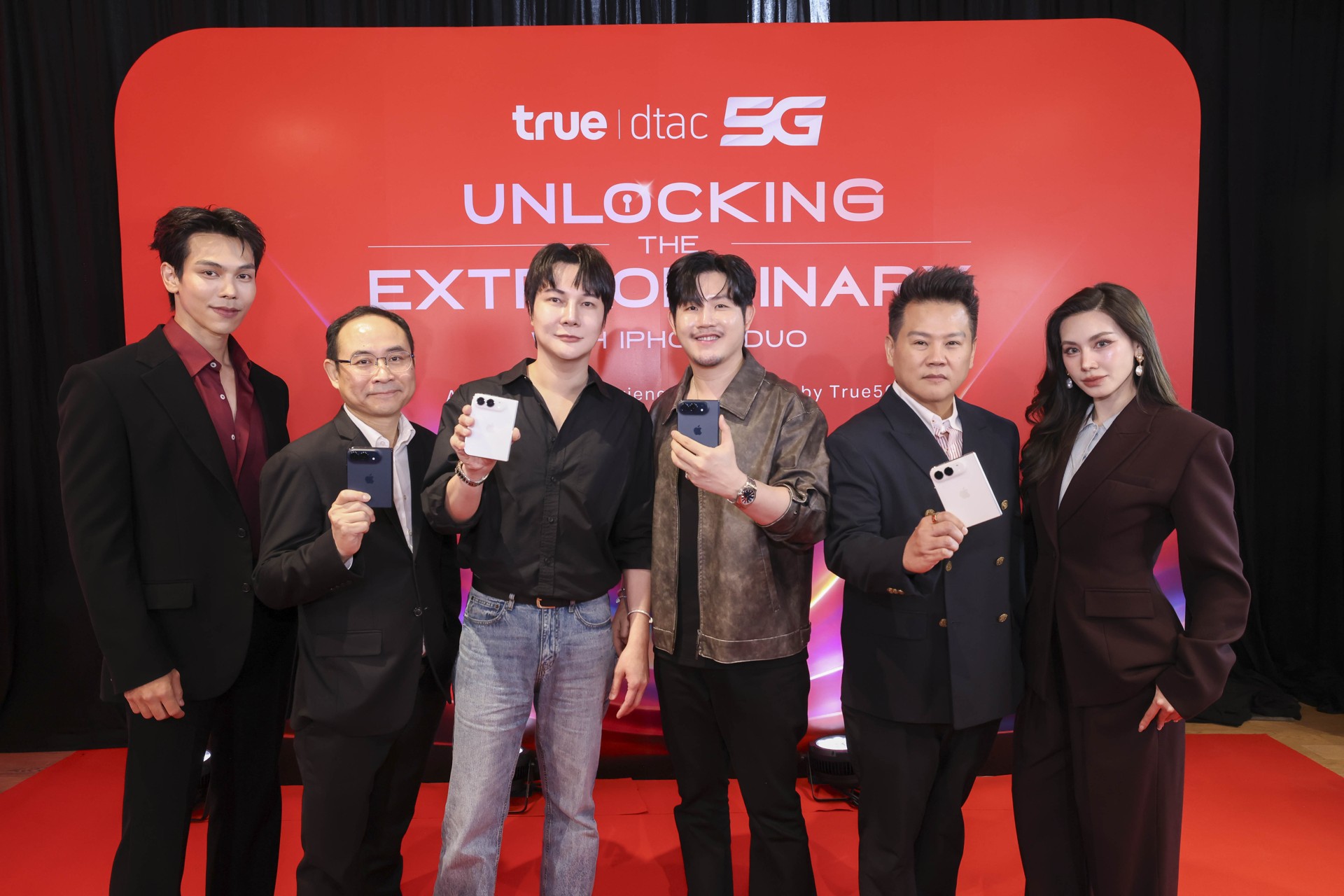 ผู้บริหารทรูและผู้ร่วมงานยืนถือ iPhone Duo หน้าฉากกิจกรรมสีแดง