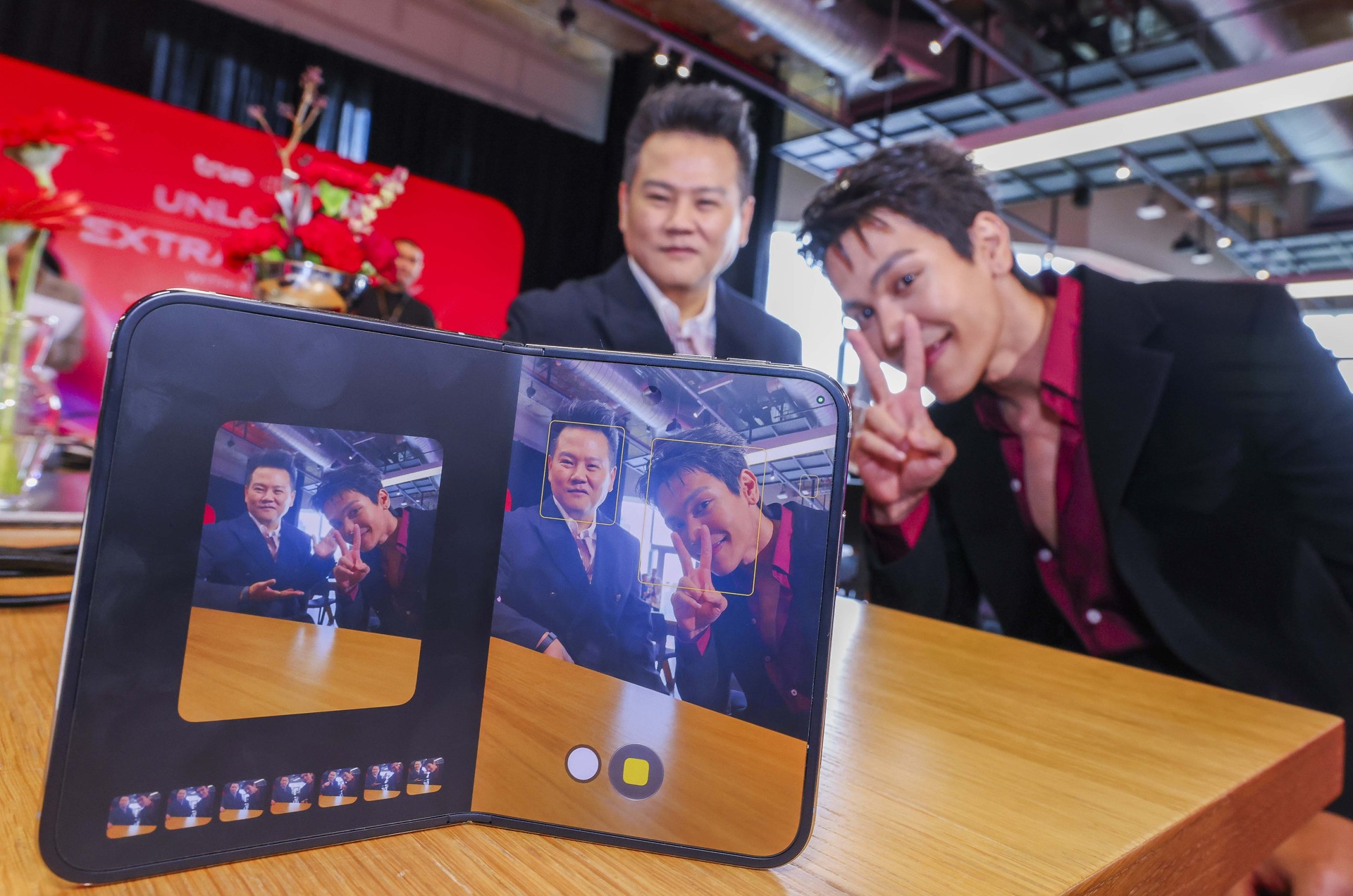 ผู้ร่วมงานสองคนโพสท่าหน้า iPhone Duo ที่เปิดแอปกล้อง