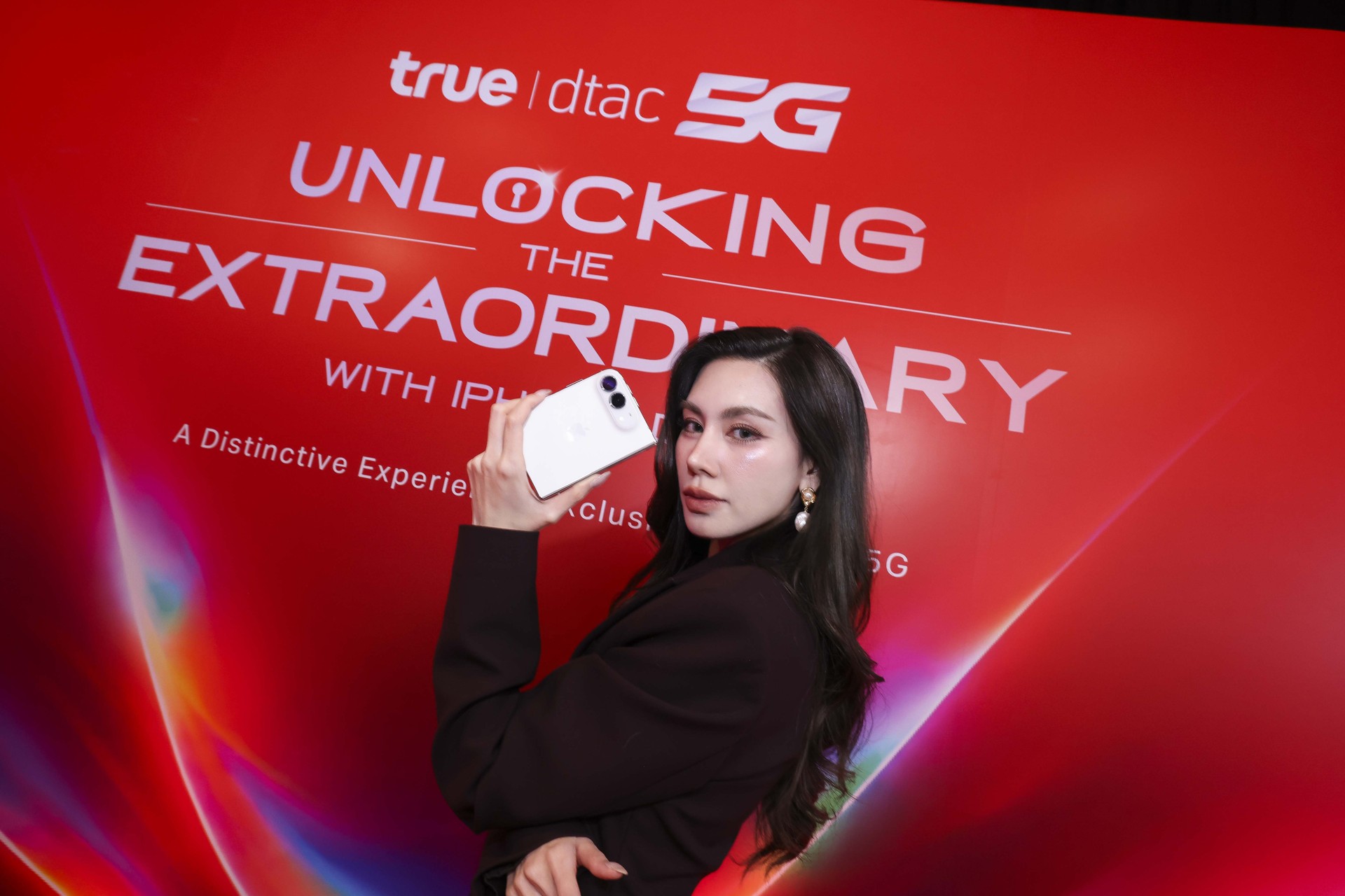 ผู้ร่วมงานถือ iPhone Duo หน้าฉาก UNLOCKING THE EXTRAORDINARY สีแดง